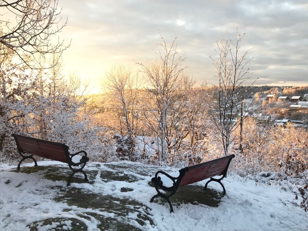 Utsiktsbild över snötäckt naturmark. Två sittbänkar finns också med. 