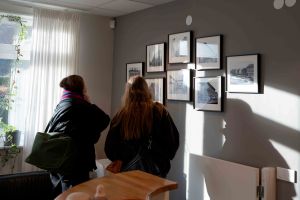 Två kvinnor studerar foton på en vägg.