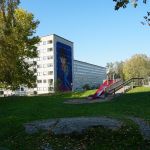 Bilden visar grönytor med ett höghus i bakgrunden.