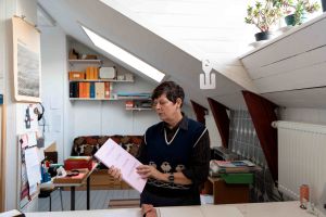 En kvinna står i en atelje och tittar på en bok hon har i handen.