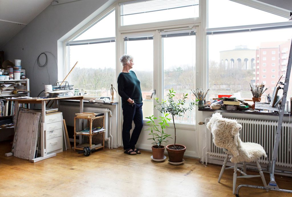 Bilden visar en kvinna som står i sin lägenhet och ser ut mot Guldhedstornet