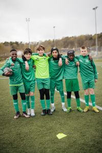 Sex pojkar i fotbollskläder står bredvid varandra och ler in i kameran.