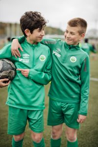 Två pojkar i fotbollskläder tittar på varandra och ler.